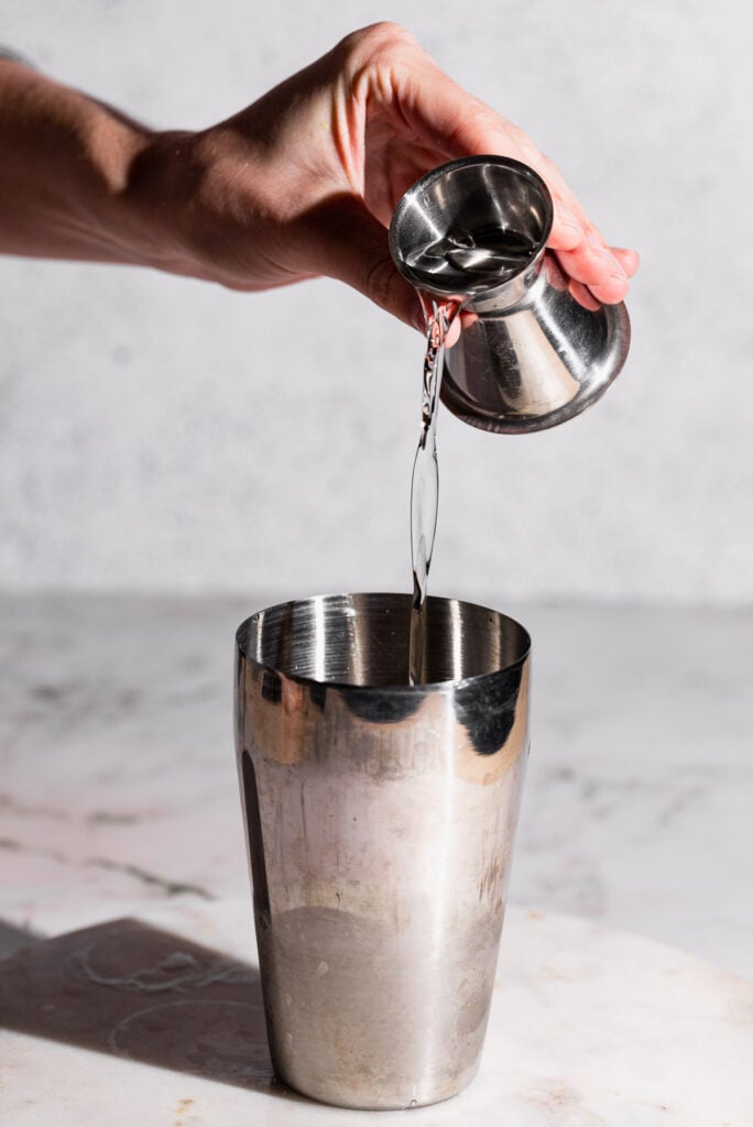 White rum pouring from a jigger into a cocktail shaker.