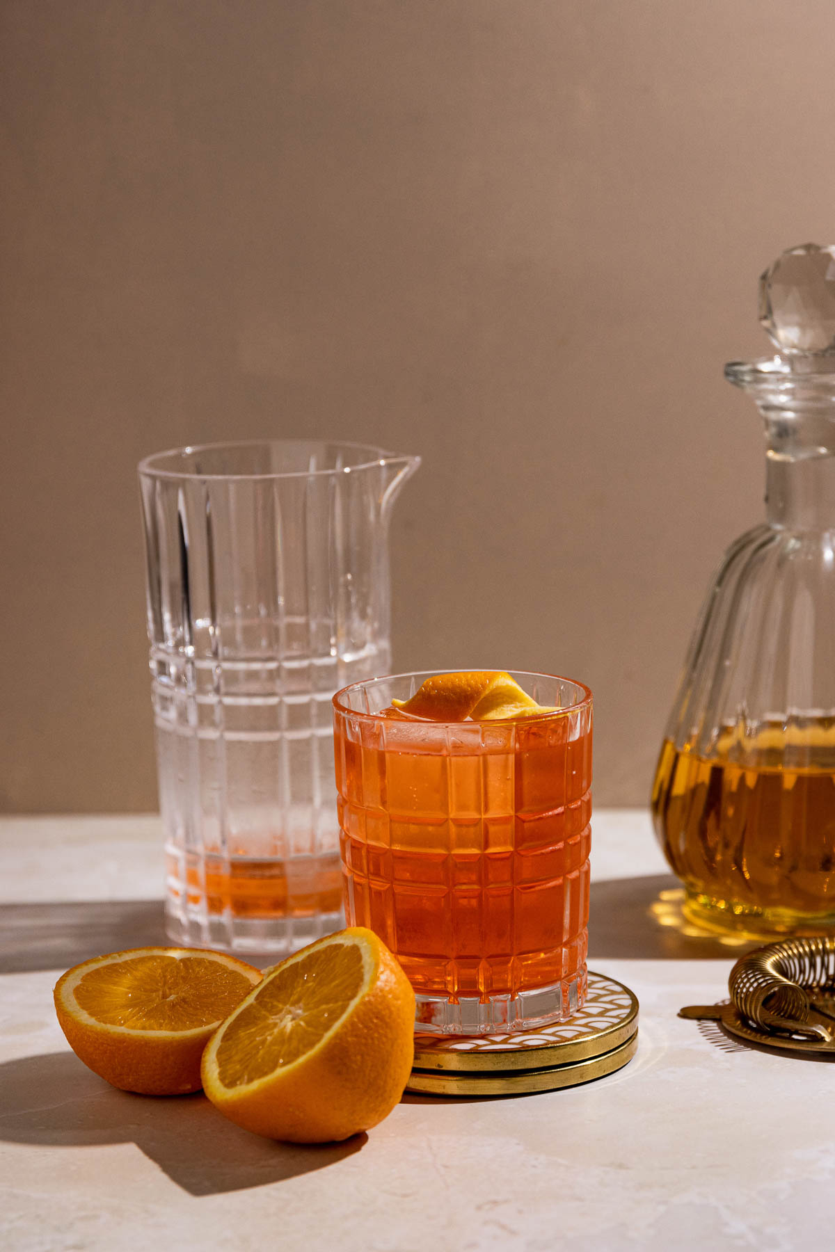 A bright orange negroni on a counter with oranges and a cocktail shaker. 