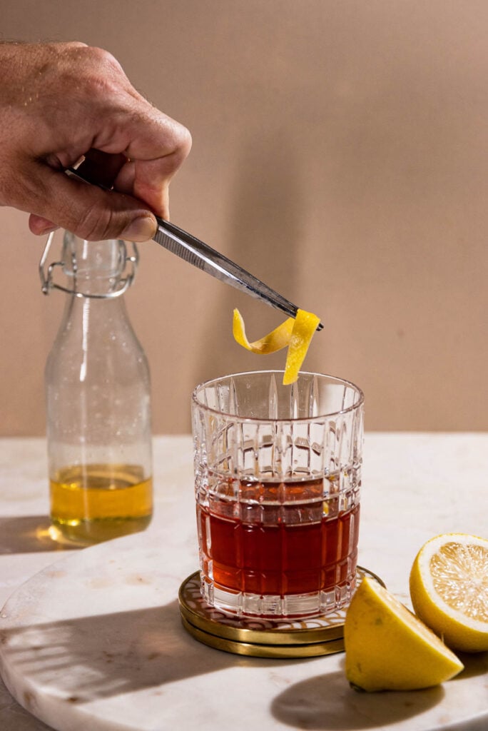 Tweezers placing lemon twist in a cocktail. 