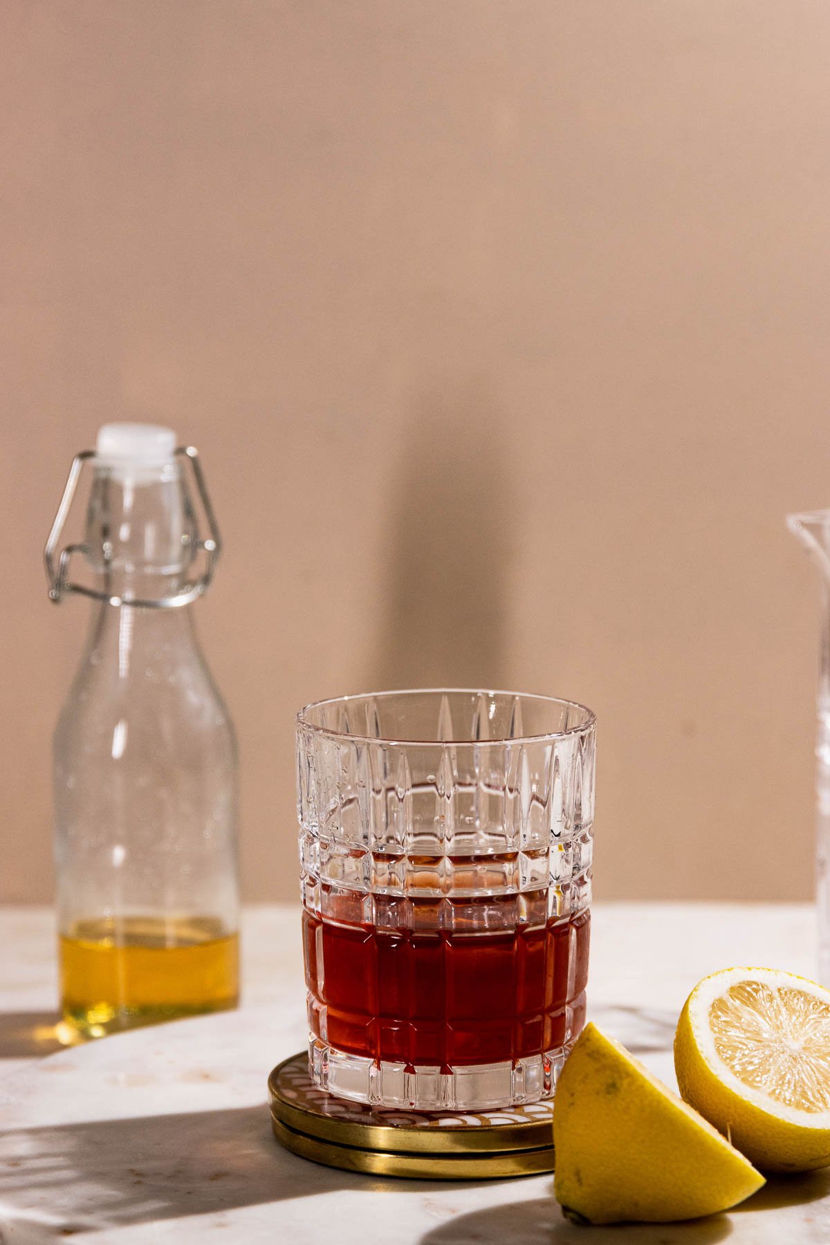 Sid shot of a classic sazerac cocktail on a table with lemons and other ingredients. 