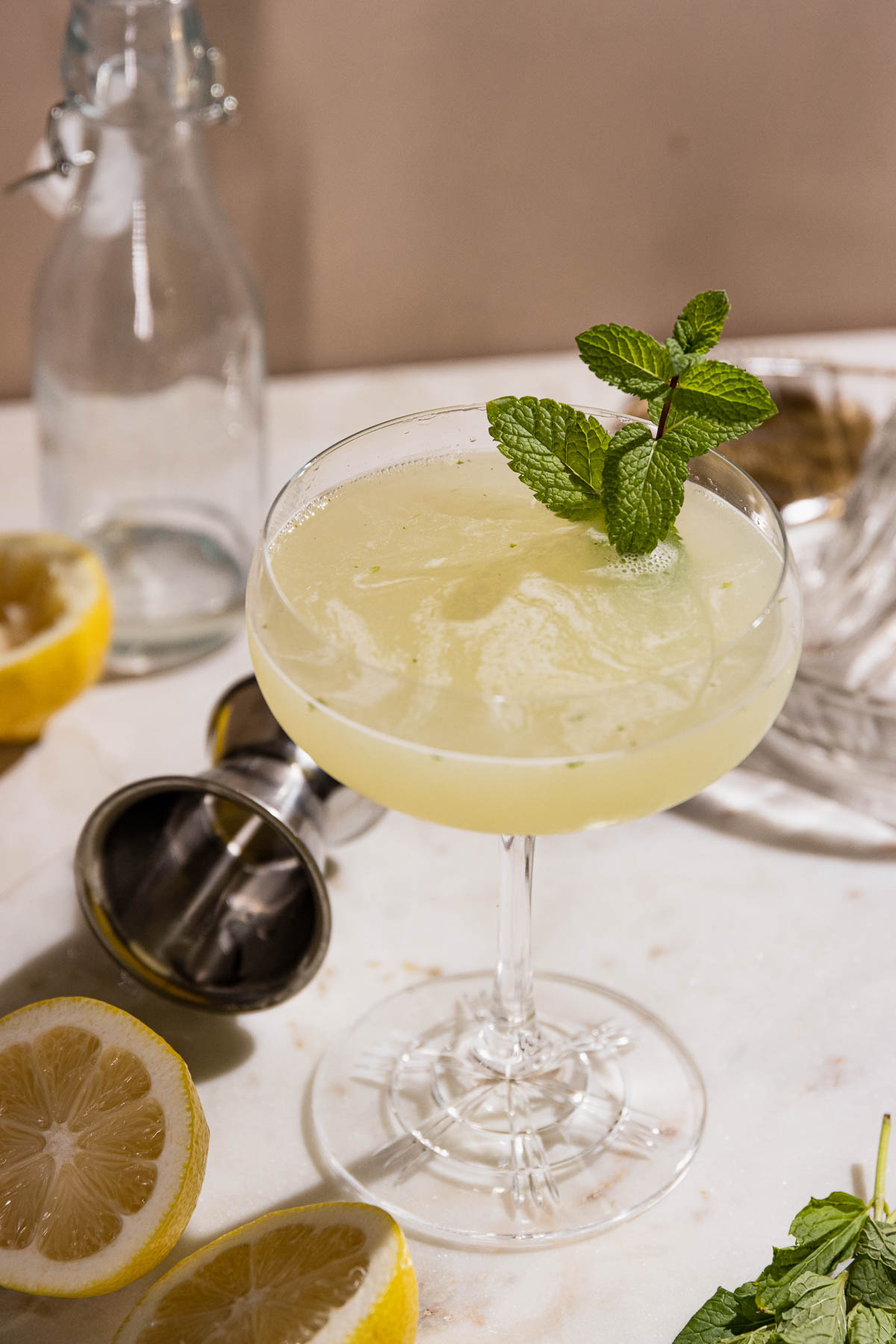 Mint sprig in a smooth southside cocktail with cocktail jigger and lemon on table. 