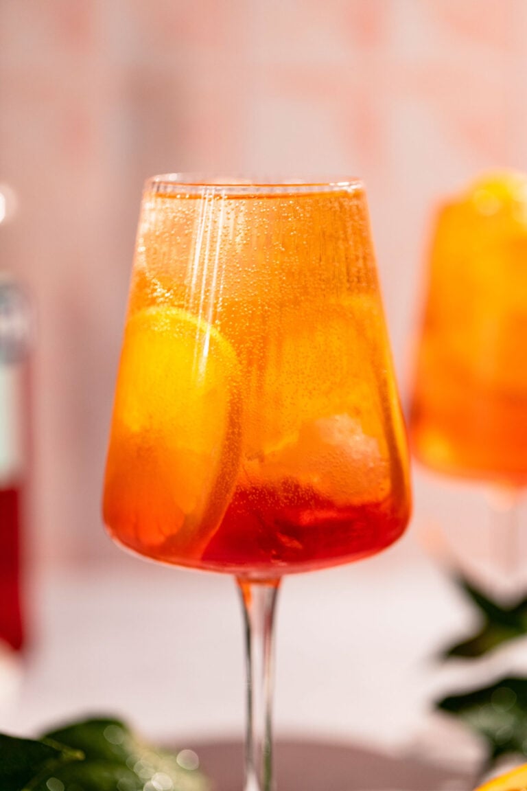 Beautiful ombre orange campari spritz cocktail in a glass with ice and orange slices.