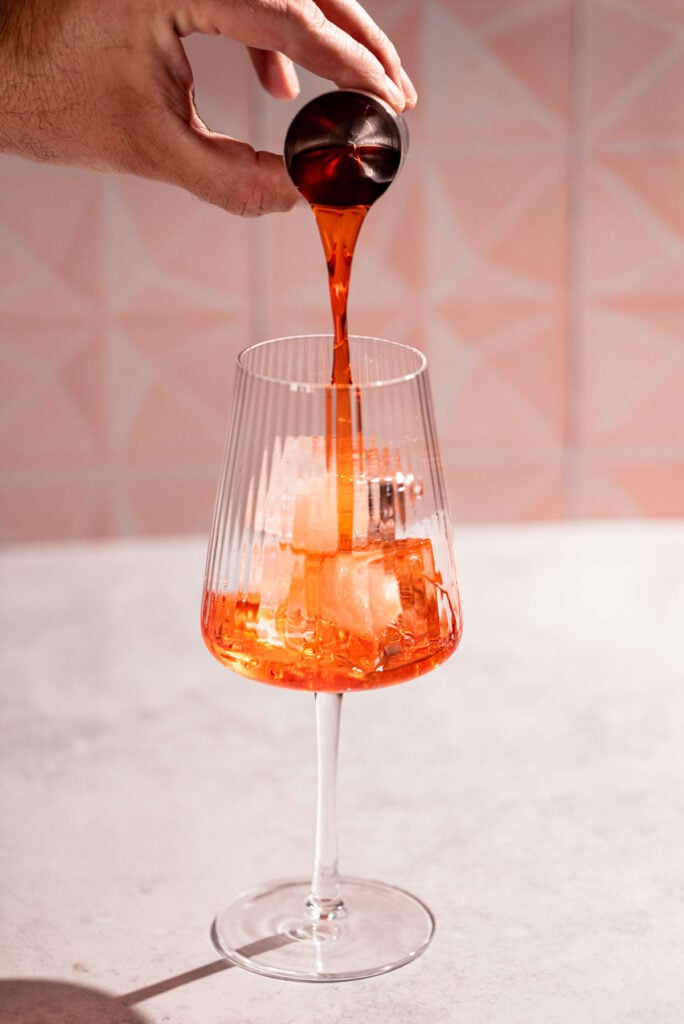 Campari being added to the wine glass. 