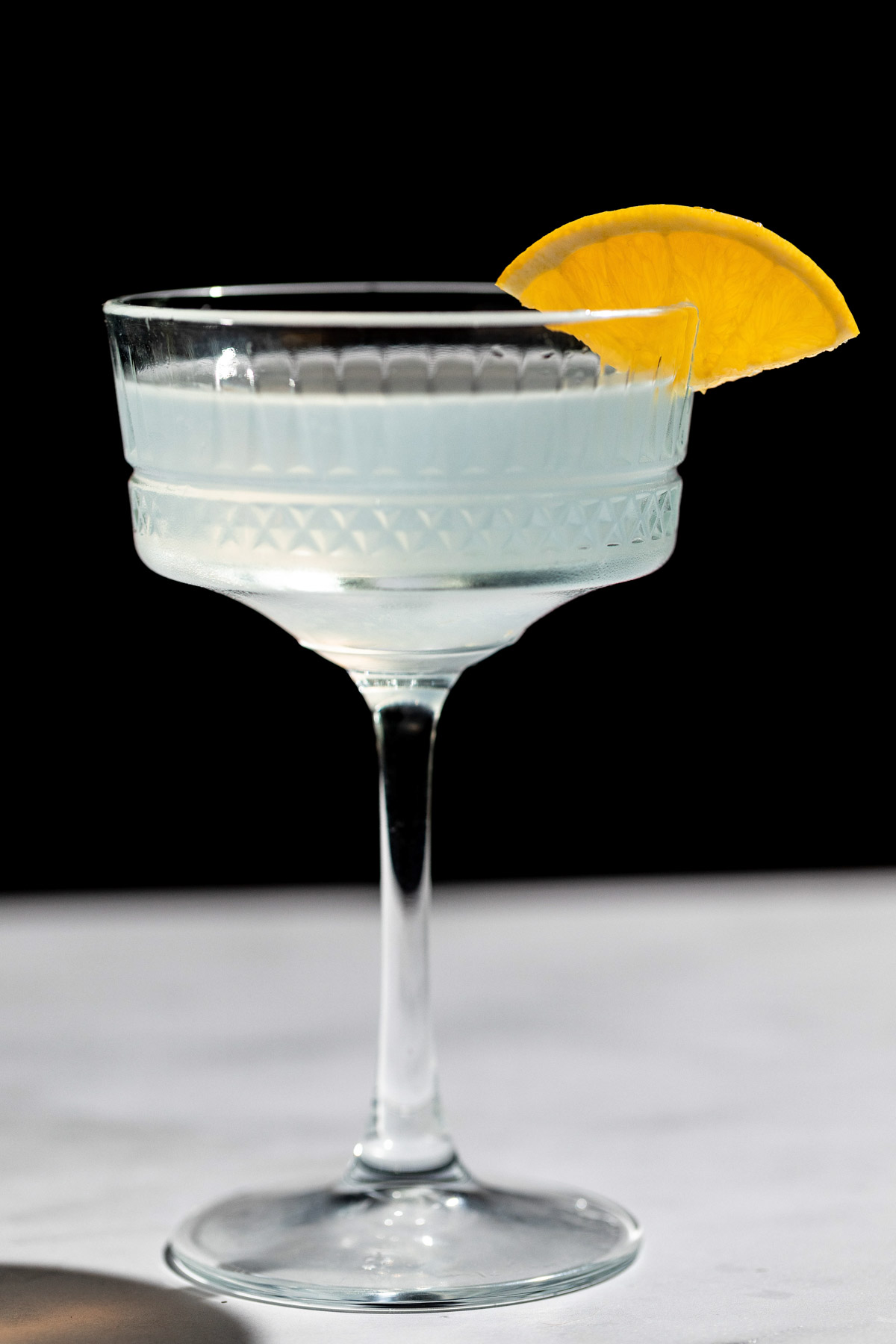 Corpse reviver cocktail in a decorative cocktail glass with an orange wedge on the rim for garnish. 