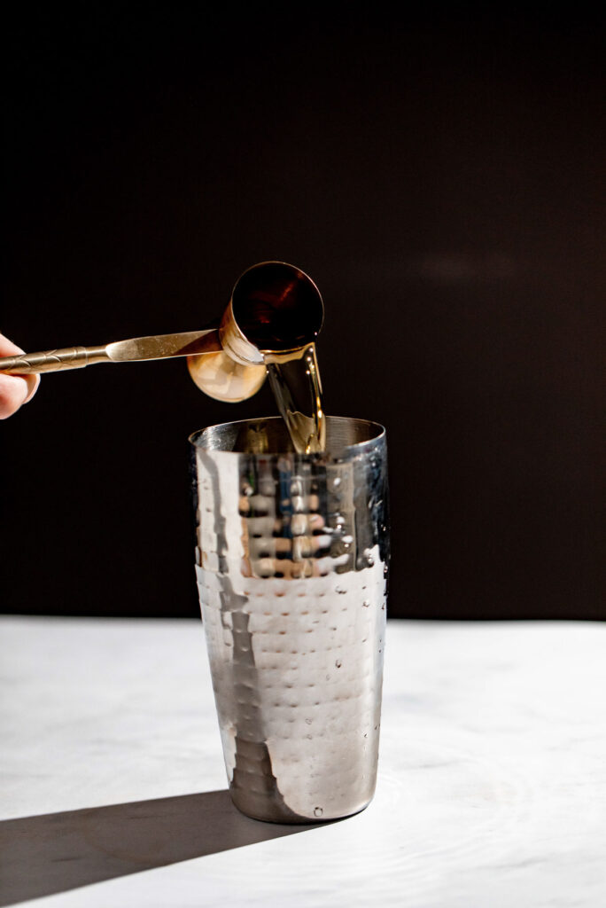 Orange liquor being added to a cocktail shaker. 