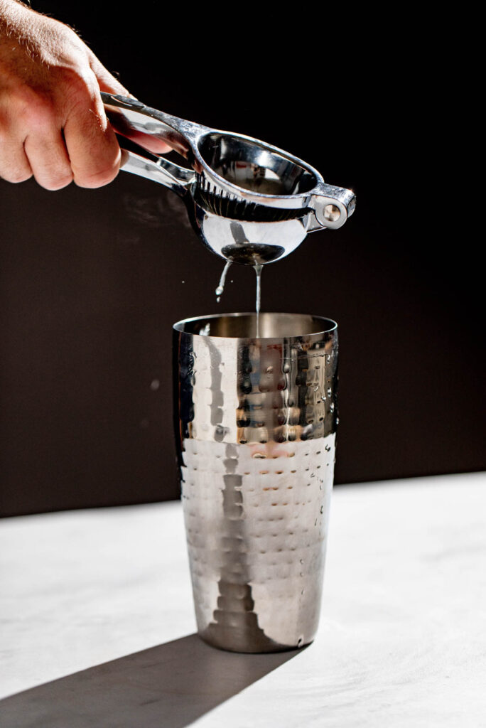 Lemon juice being squeezed into a cocktail shaker. 