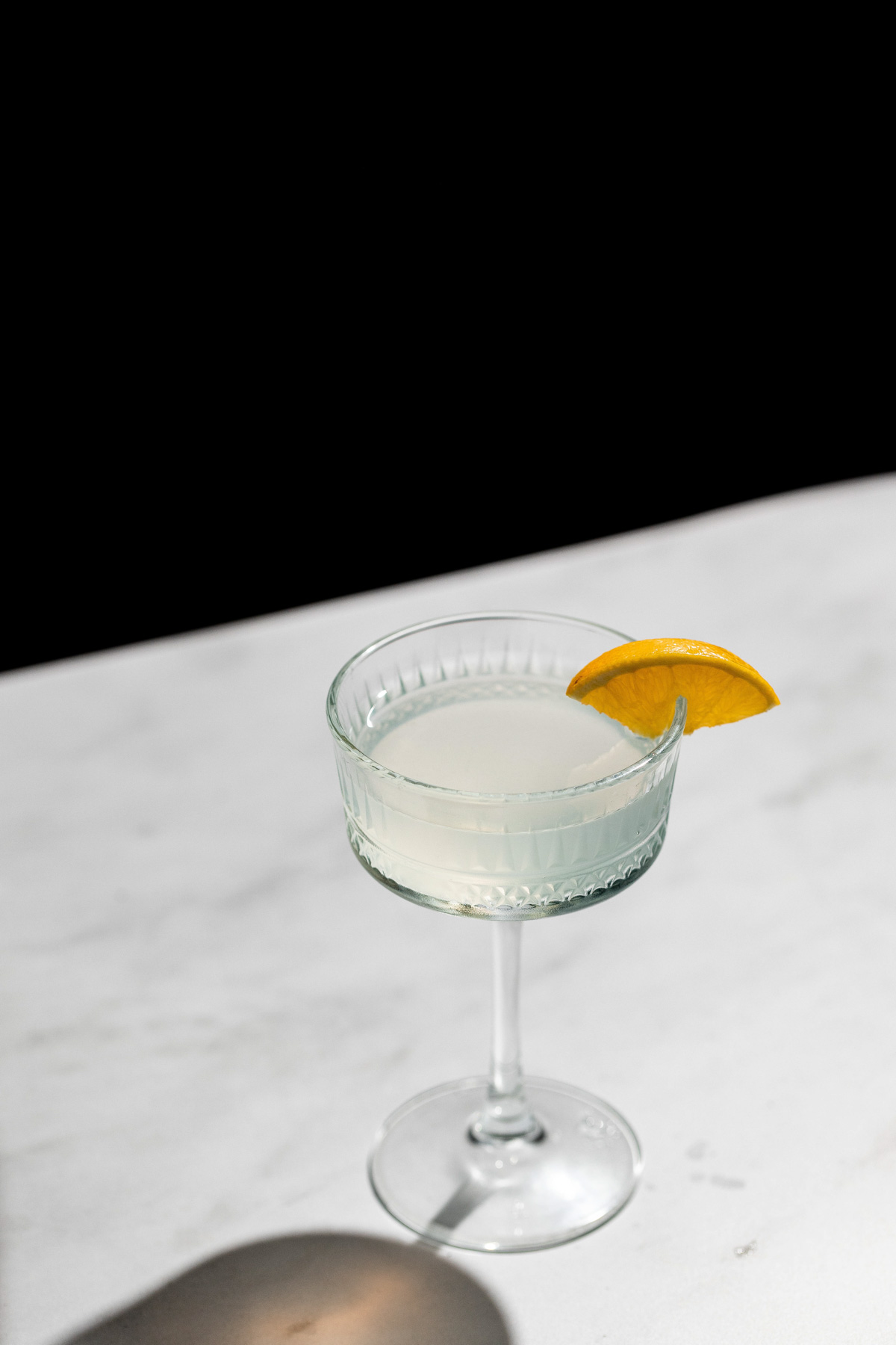 A crystal coupe glass with a corpse reviver cocktail and orange wedge. 