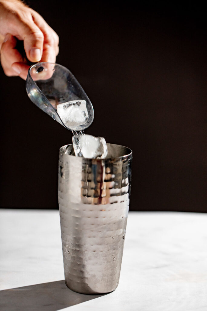 Ice being added to a cocktail shaker. 