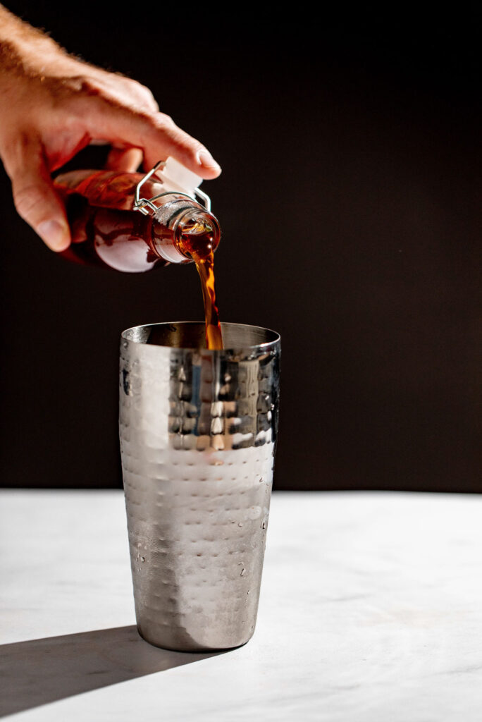 Earl grey simple syrup being added to a cockatil shaker. 