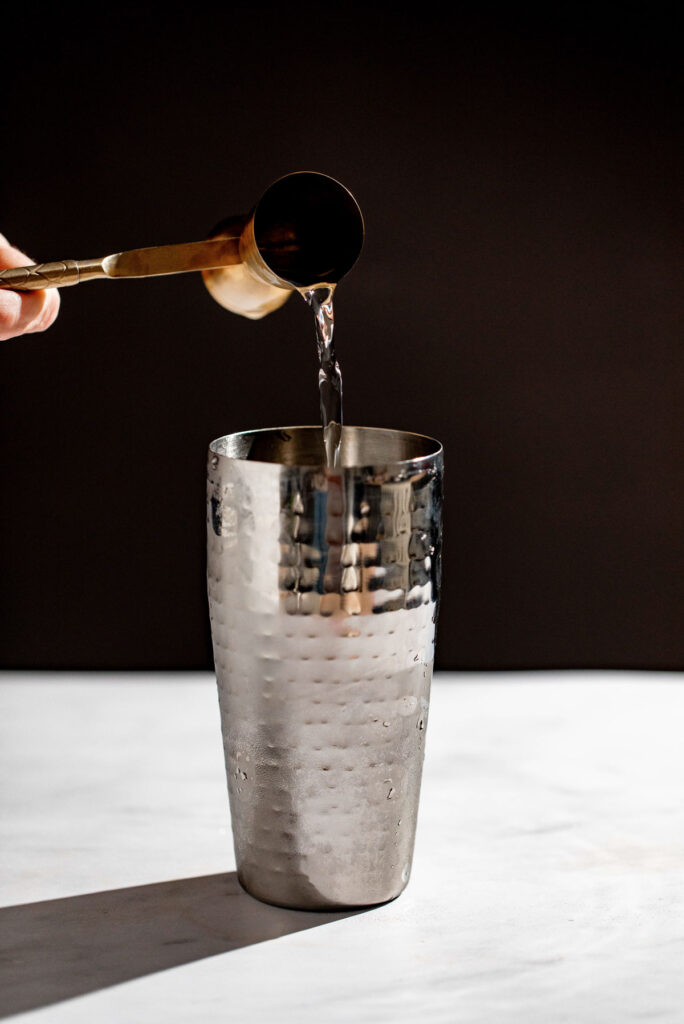 Gin being added to a cocktail shaker. 