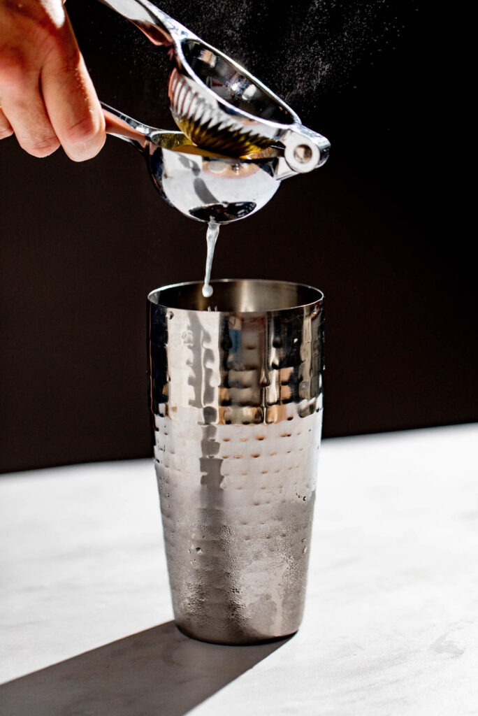 Lemon juice being squeezed into a cocktail shaker. 