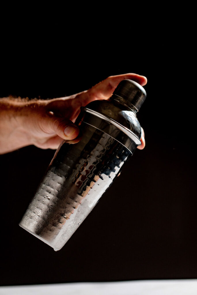 Hand shaking a cocktail shaker, showing the chilled outter layer. 