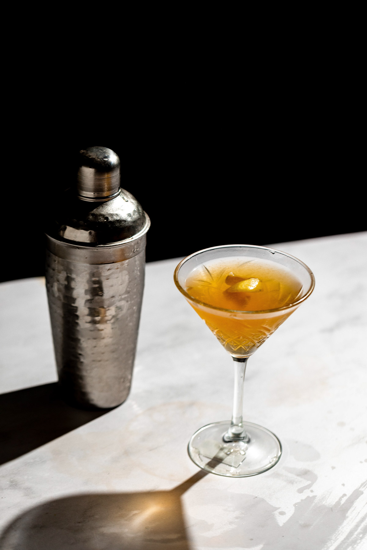 Crystal glass filled with this martini recipe casting a long shadow on a white table. 