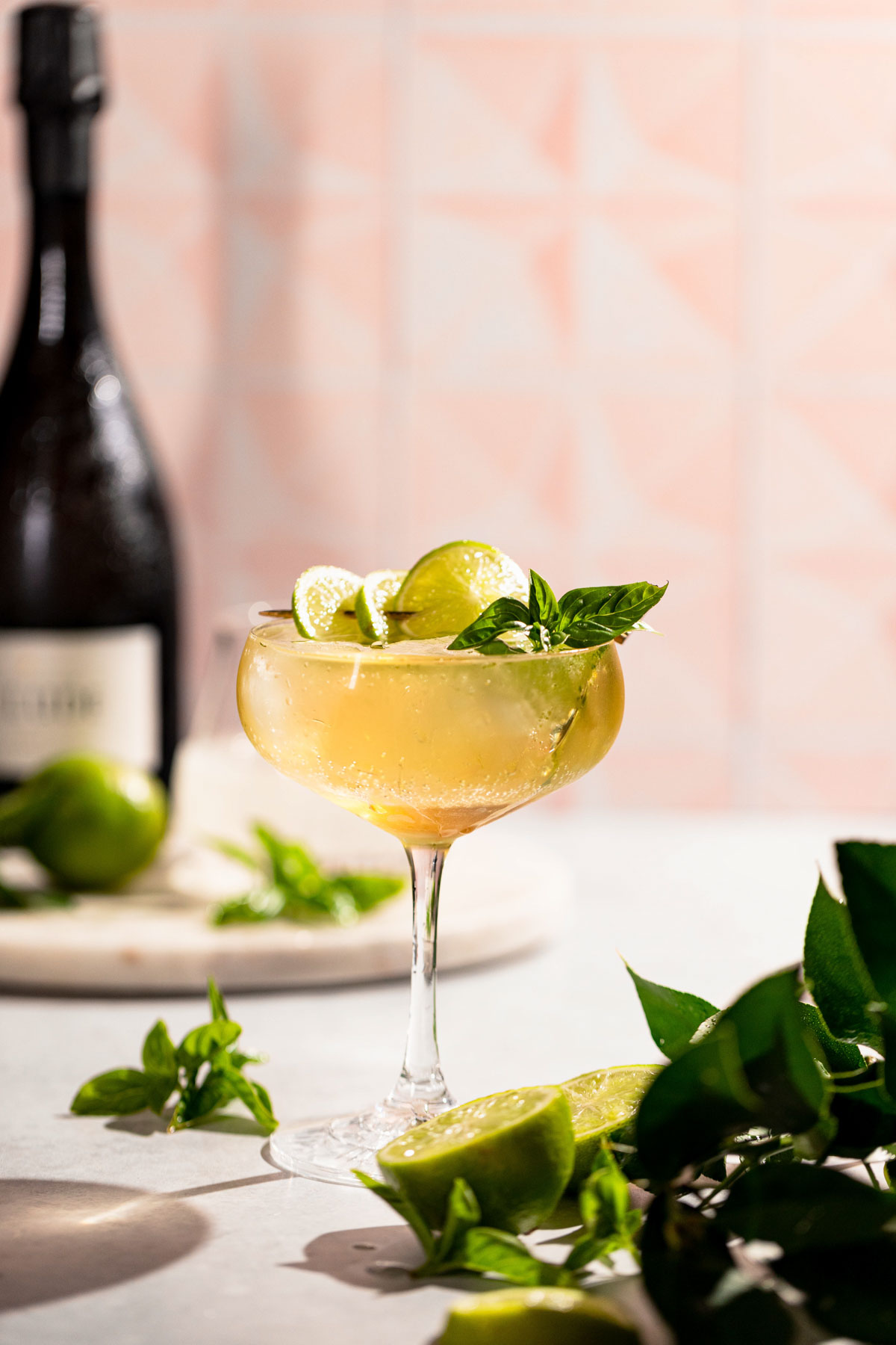 Coupe glass filled to the rim with a light hugo spritz cocktail garnished with lime and basil. 
