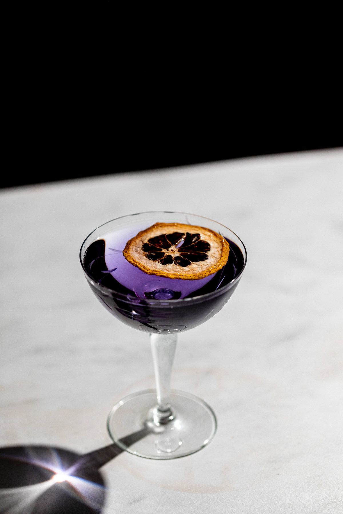 Bright violet aviation cocktail in a coupe glass with a dehydrated lemon.