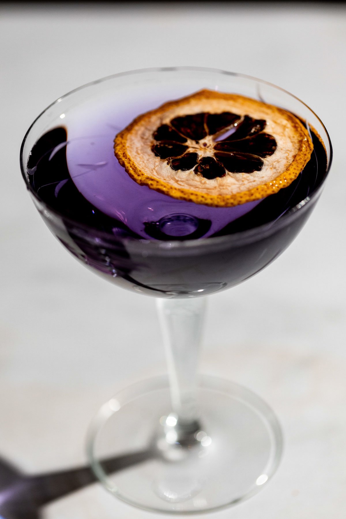 Close up of an aviation cocktail in a coupe glass with a lemon slice. 