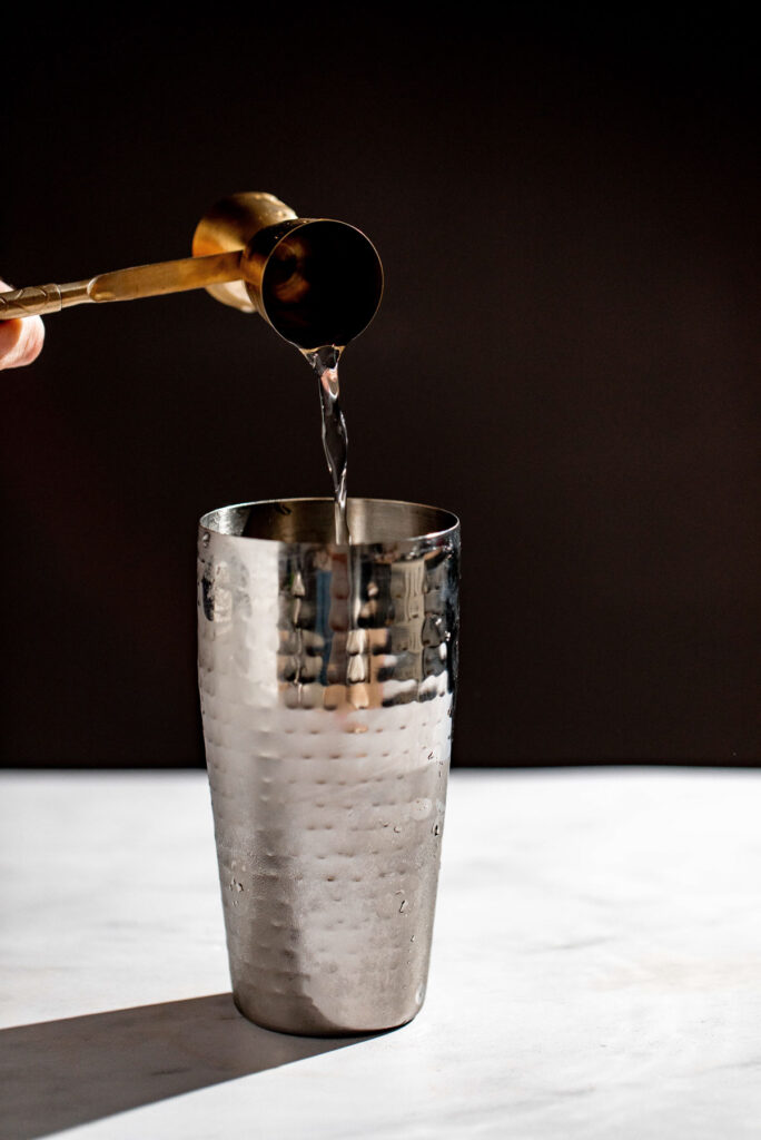 Gin being added to a cocktail shaker. 