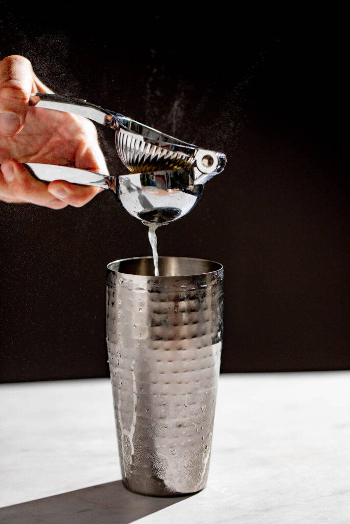 Lemon juice being squeezed into a cocktail shaker. 