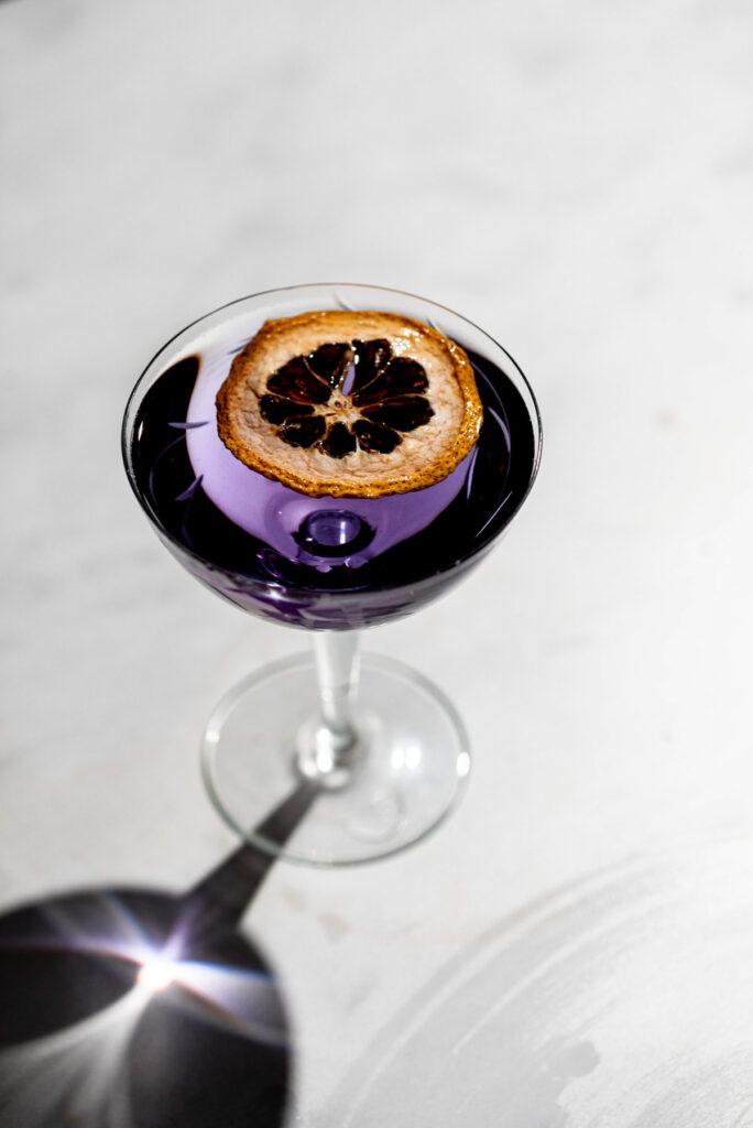 Purple aviation cocktail in a coupe glass on a white table. 