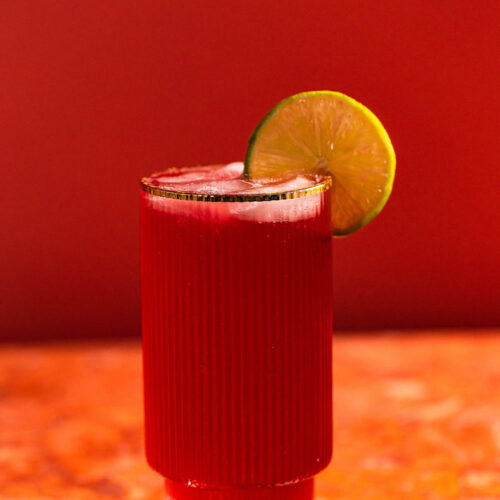 Bright red el diablo cocktail garnished with a lime wedge in a cocktail glass.