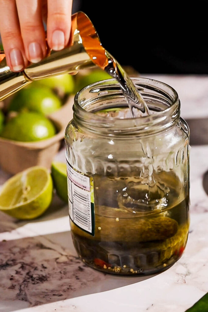 Tequila being poured into a pickle jar.