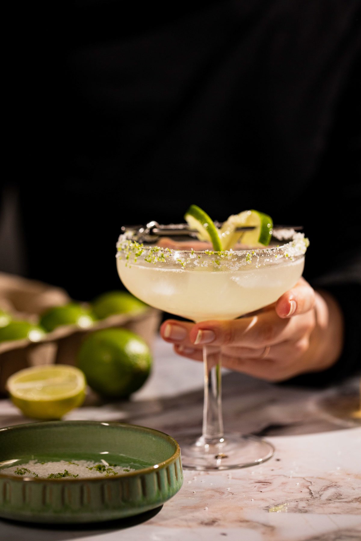 Handing holding a mezcal cocktail in a coupe glass.