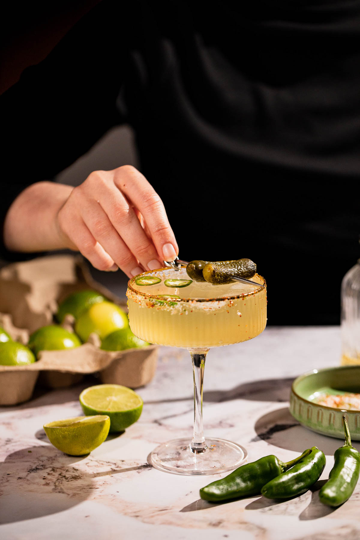 Hand placing cocktail pick with gherkins over a margarita.