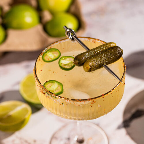 close up of a pickle margarita garnished with gherkins on a cocktail pick.