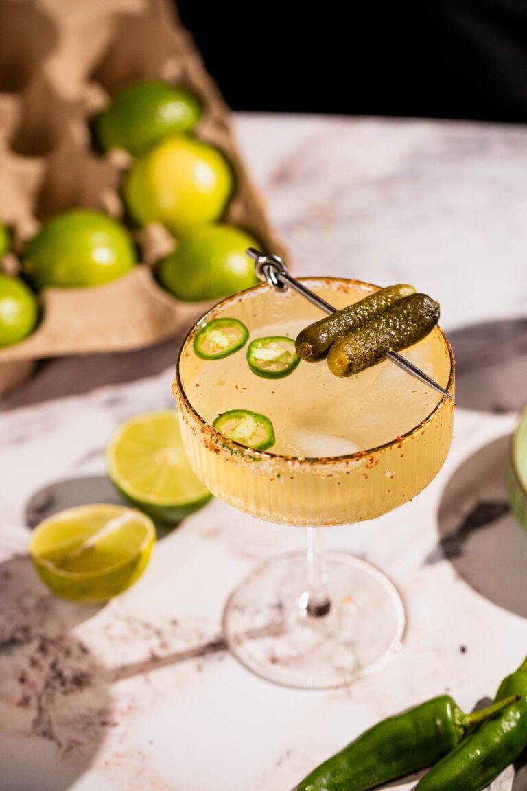 Pickle margarita in a cocktail glass, garnished with jalapeno slices and pickles.