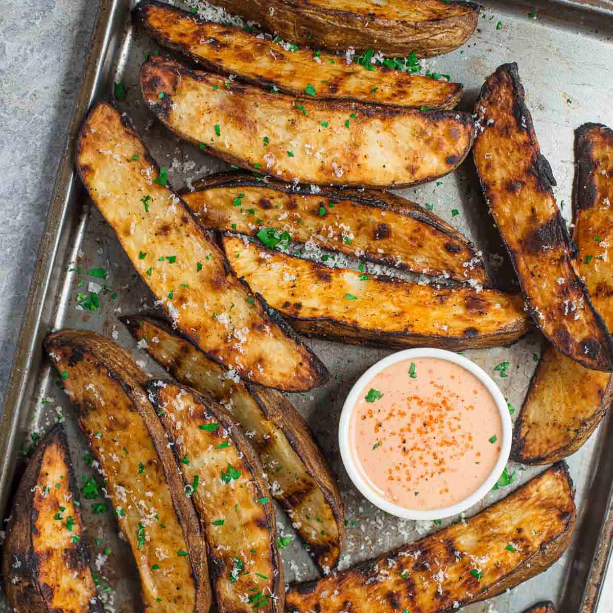 Potato wedges on a platter with sauce. 