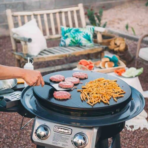 Hand flipping a burger on a griddle. 